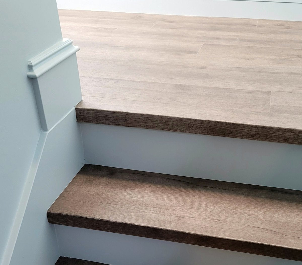 Wooden staircase with a light gray wall and wooden handrail.